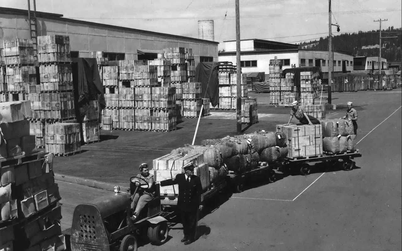 A photograph at the Velox Naval Supply Depot in 1944. Workers are moving pallets with a tractor.